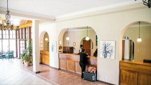 A reception area with a wooden counter, a receptionist, and a guest with a suitcase.