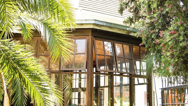A conservatory with glass walls, a wooden floor, and a seating area with chairs and tables. - The Bronte Garden Hotel (Harare)