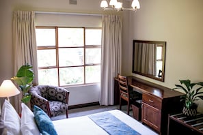 Quarto de hotel com cama, escrivaninha, cadeira, espelho e janela com cortinas.