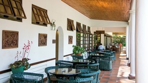 A covered outdoor seating area with wicker furniture, wooden ceiling, and decorative wall panels.