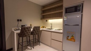 A compact kitchen with a microwave, refrigerator, and two bar stools. - Skyline Hotel & Suite (Tabuk)