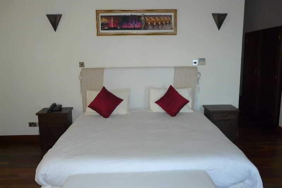Una habitación de hotel con una cama, dos mesitas de noche, un cuadro en la pared y una puerta.