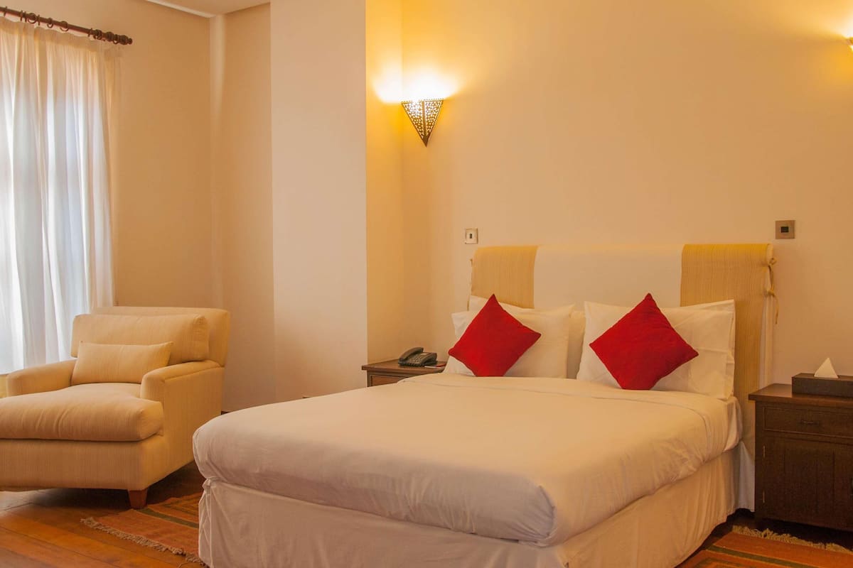 A hotel room with a bed, a chair, a nightstand, and a wall-mounted light fixture.