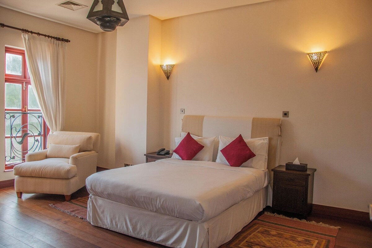 A bedroom with a large bed, a chair, bedside tables, and a window with curtains.