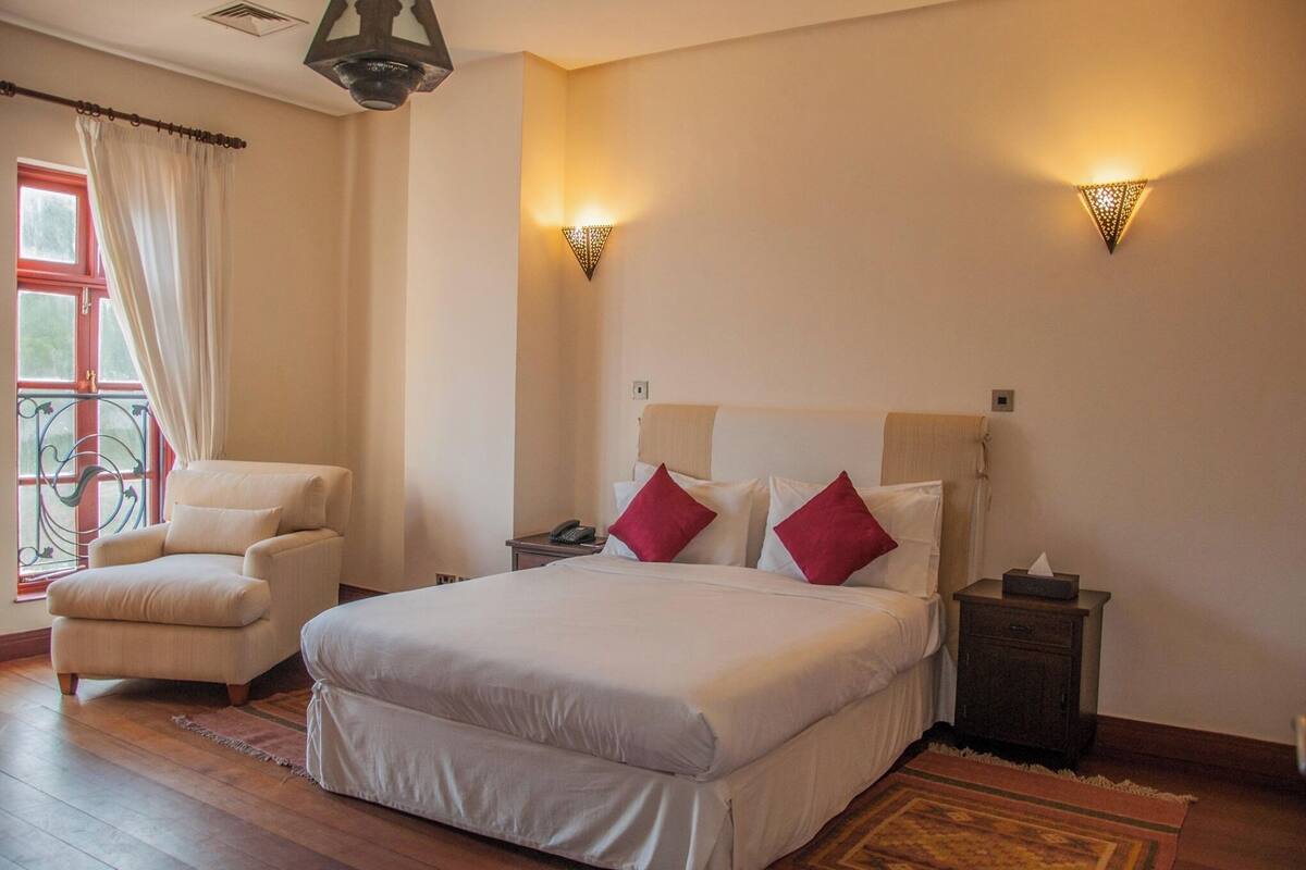 A bedroom with a large bed, a chair, bedside tables, and a window with curtains.