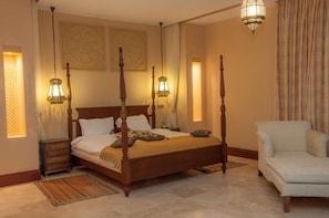 A four-poster bed with a wooden frame, a bedside table, a chair, and two wall-mounted lamps.
