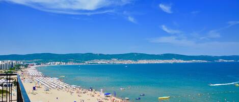 A beach with umbrellas and people, a clear sky, and a view of the sea and distant buildings.