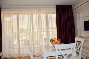 A dining area with a table and chairs, a fruit bowl on the table, and a view through sheer curtains. - Golden Rainbow (Nessebar)