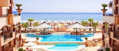 A pool area with a view of the beach and ocean, surrounded by buildings.