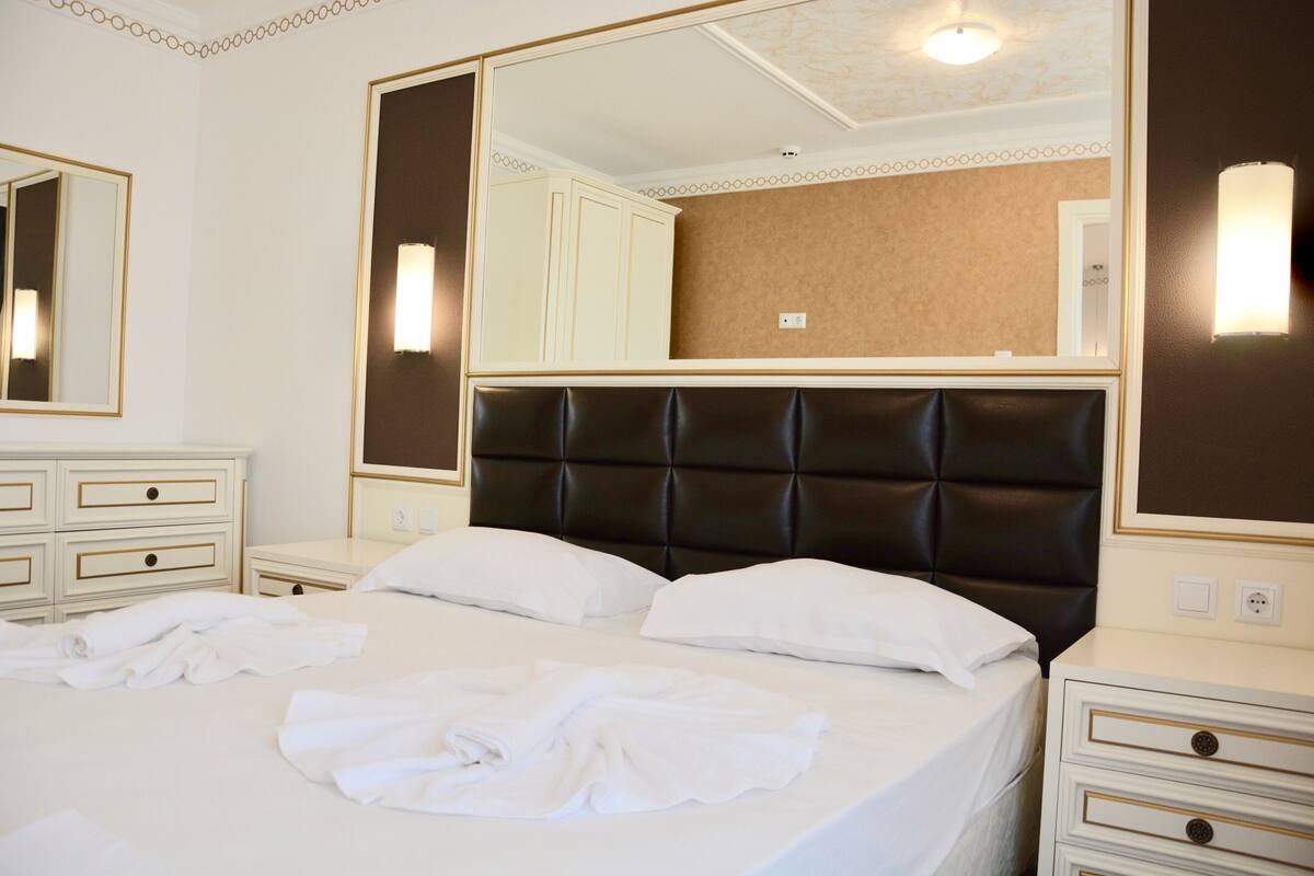 A hotel room with a large bed, two bedside tables, a wardrobe, and a large mirror.