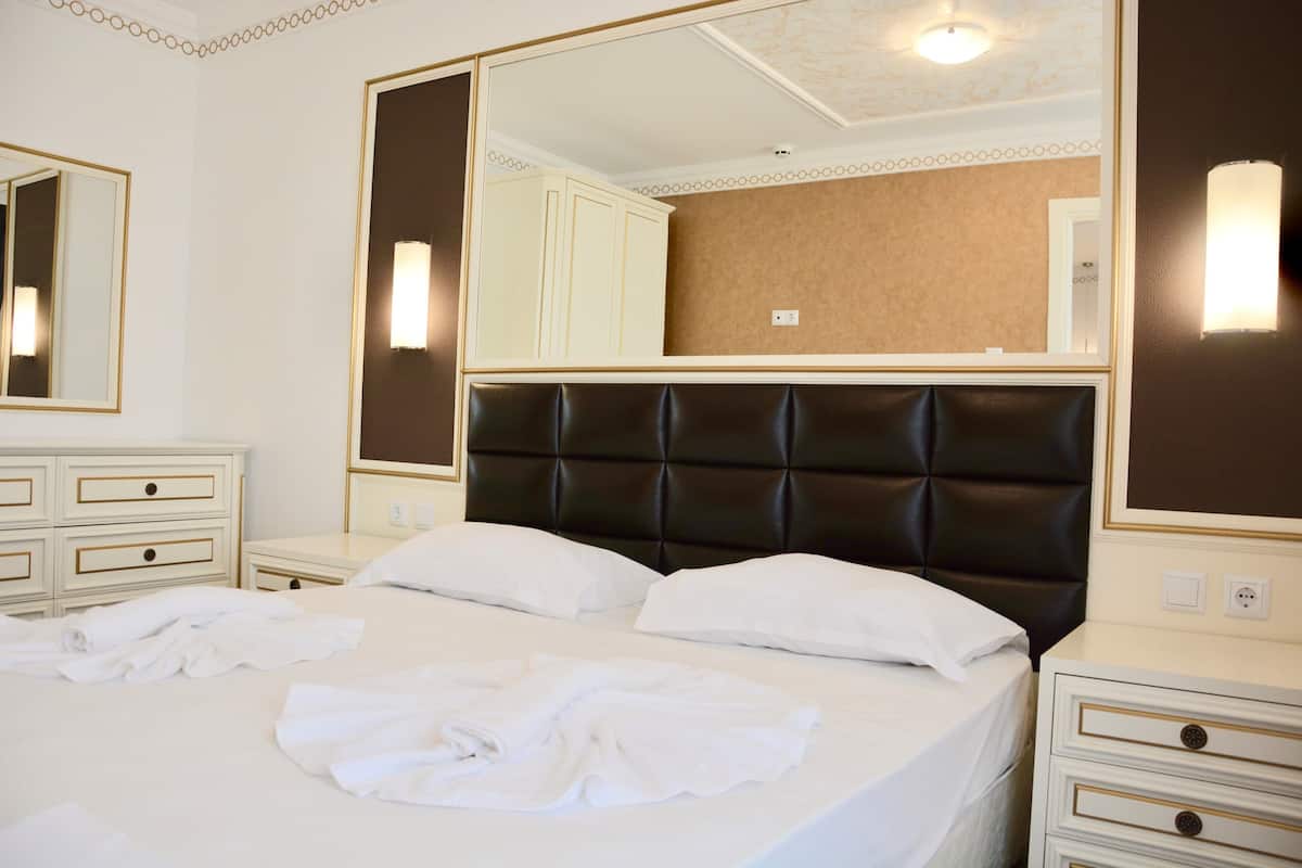 Una habitación de hotel con una cama grande, dos mesitas de noche, un espejo y una lámpara fijada a la pared.