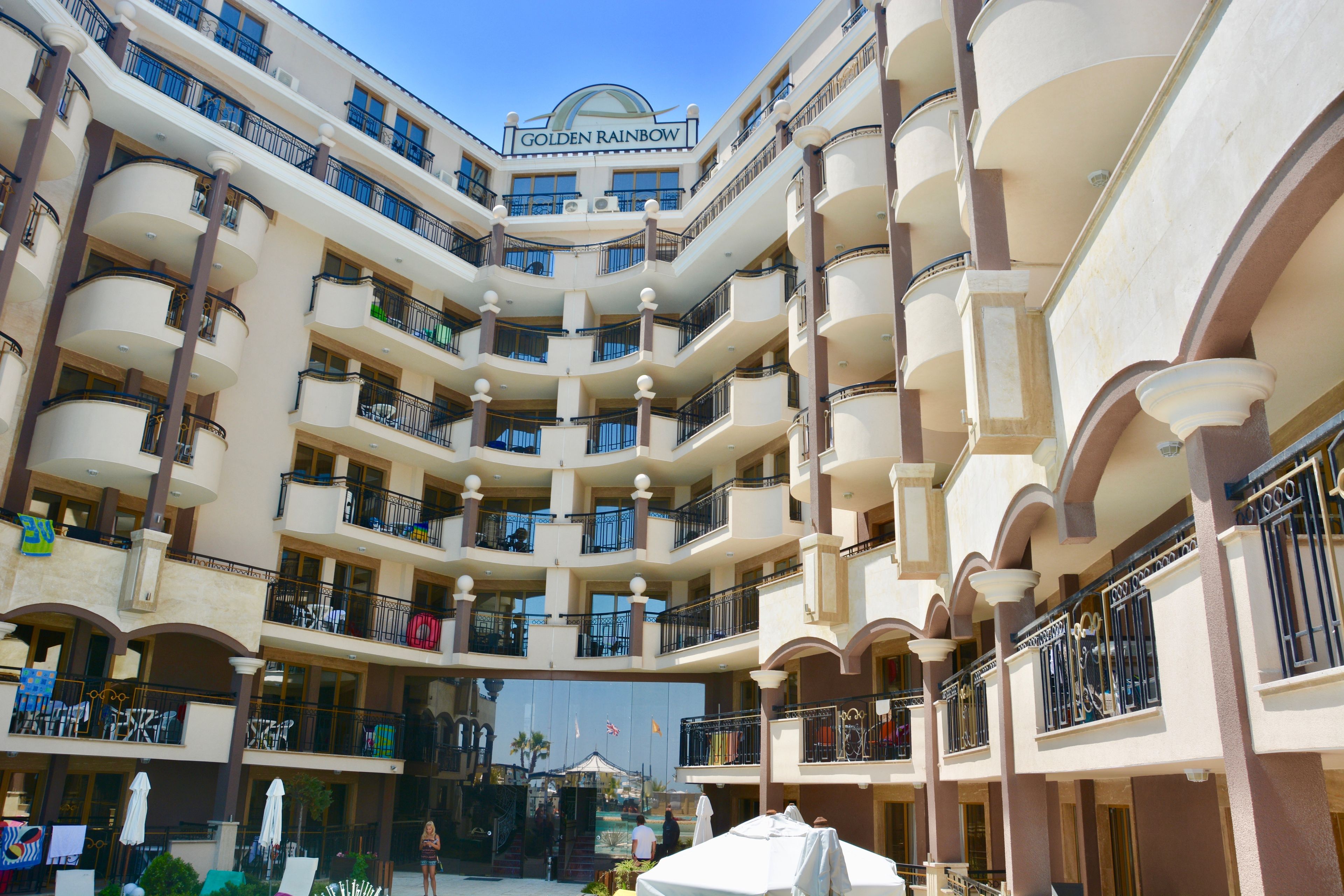 Un hôtel à plusieurs étages, doté de balcons, d’un atrium central et d’une enseigne indiquant « Golden Rainbow ».