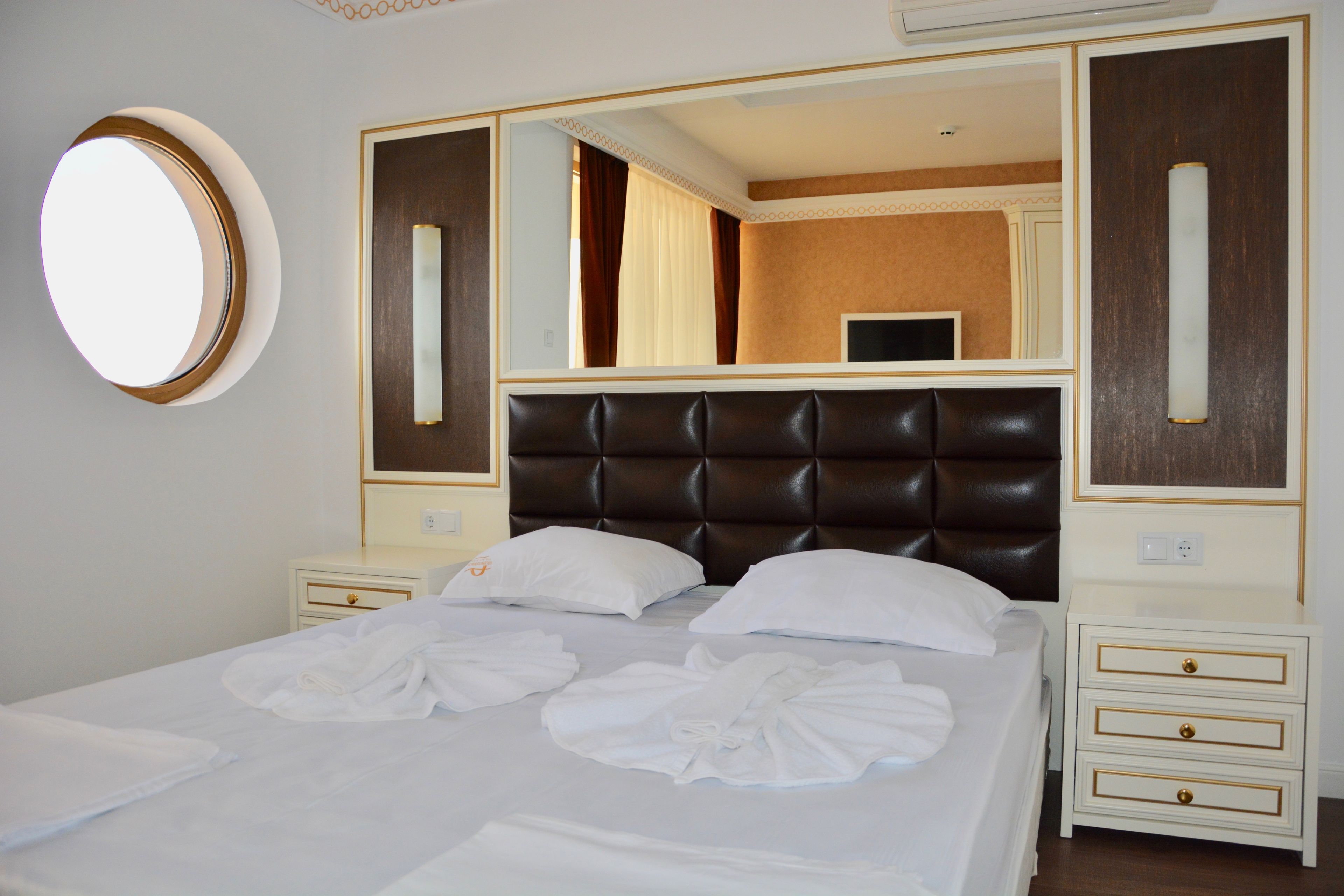 Quarto de hotel com uma cama grande, um espelho redondo e uma televisão.