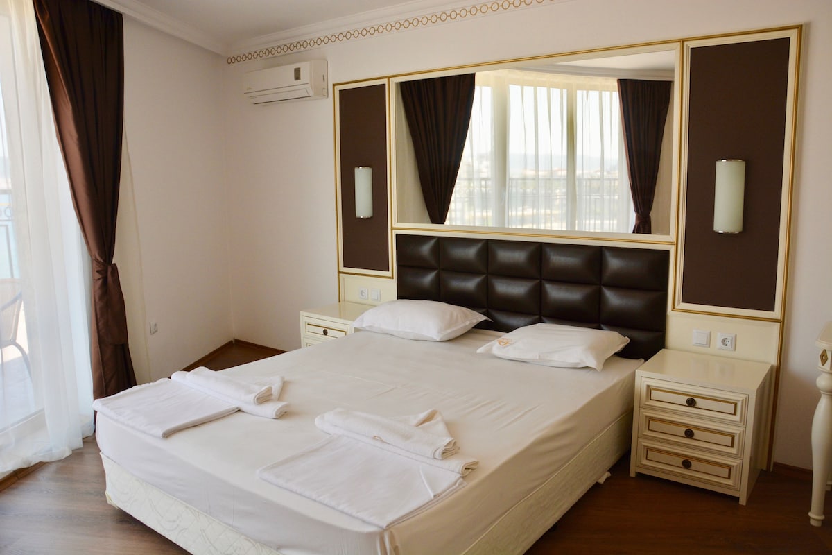 A hotel room with a large bed, two bedside tables, a mirror, and a window with curtains.