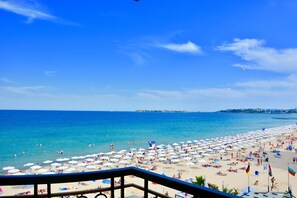 A beach with umbrellas and people, a clear sky, and a view of the sea. - Golden Rainbow (Nessebar)