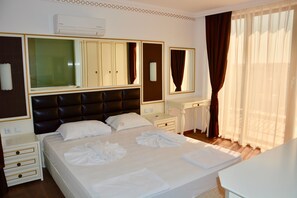 Une chambre d’hôtel avec un grand lit, une table de chevet, une commode, un miroir et une fenêtre avec des rideaux.