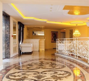 A grand lobby with a marble floor, a white reception desk, and a chandelier.