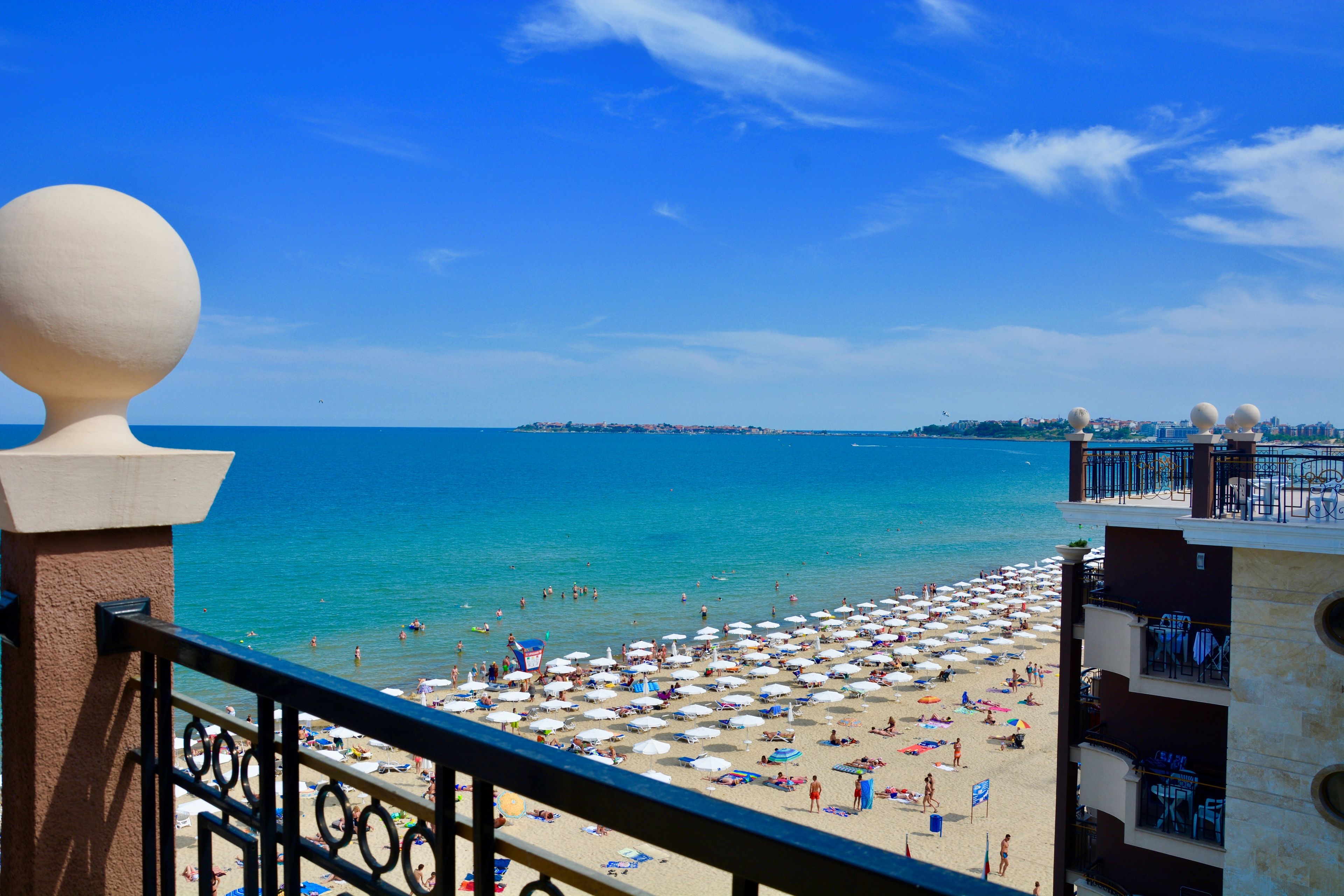 A beach with umbrellas and people, a clear sky, and a distant cityscape.