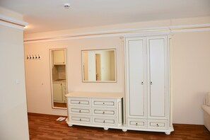 A room with a wooden floor, a white wardrobe with multiple drawers, a large mirror, and a coat rack. - Golden Rainbow (Nessebar)