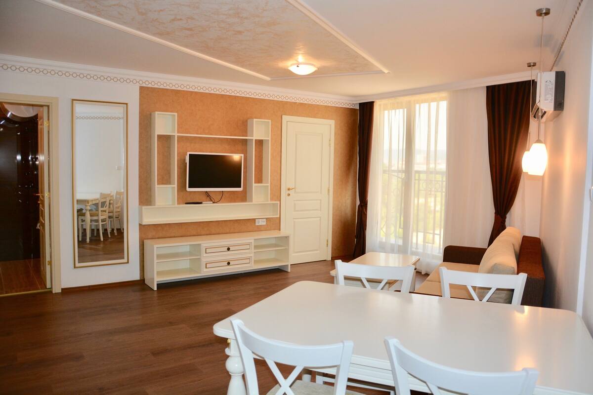 A hotel room with a dining area, a TV, a door, and a window with curtains.