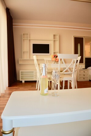 Une chambre d’hôtel avec une table blanche, une bouteille de champagne et un verre posé sur la table. Un téléviseur est fixé au mur et une chaise blanche se trouve devant le téléviseur.