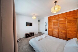 Ein Schlafzimmer mit einem Bett, einem Fernseher, einem hölzernen Kopfteil und einer Deckenleuchte.