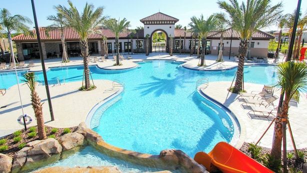 A swimming pool with a water slide, palm trees, and a building with a tiled roof. - Solterra Resort Homes (Davenport)