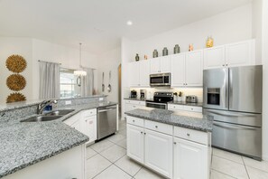 A modern kitchen with white cabinets, granite countertops, stainless steel appliances, and decorative wall art. - Solterra Resort Homes (Davenport)