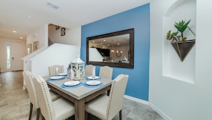 A dining area with a table set for four, chairs, a mirror, and a potted plant on the wall. - Solterra Resort Homes (Davenport)