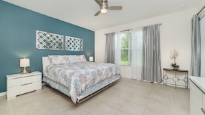 A bedroom with a bed, bedside tables, a ceiling fan, a window with curtains, and a small table with a plant. - Solterra Resort Homes (Davenport)