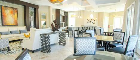 A spacious living area with a sofa, dining table, and chairs, a kitchen area, and a ceiling fan.