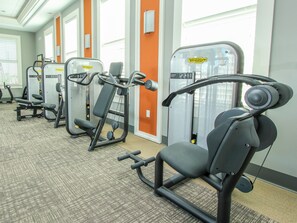 A row of exercise machines in a gym with a carpeted floor and large windows. - Solterra Resort Homes (Davenport)