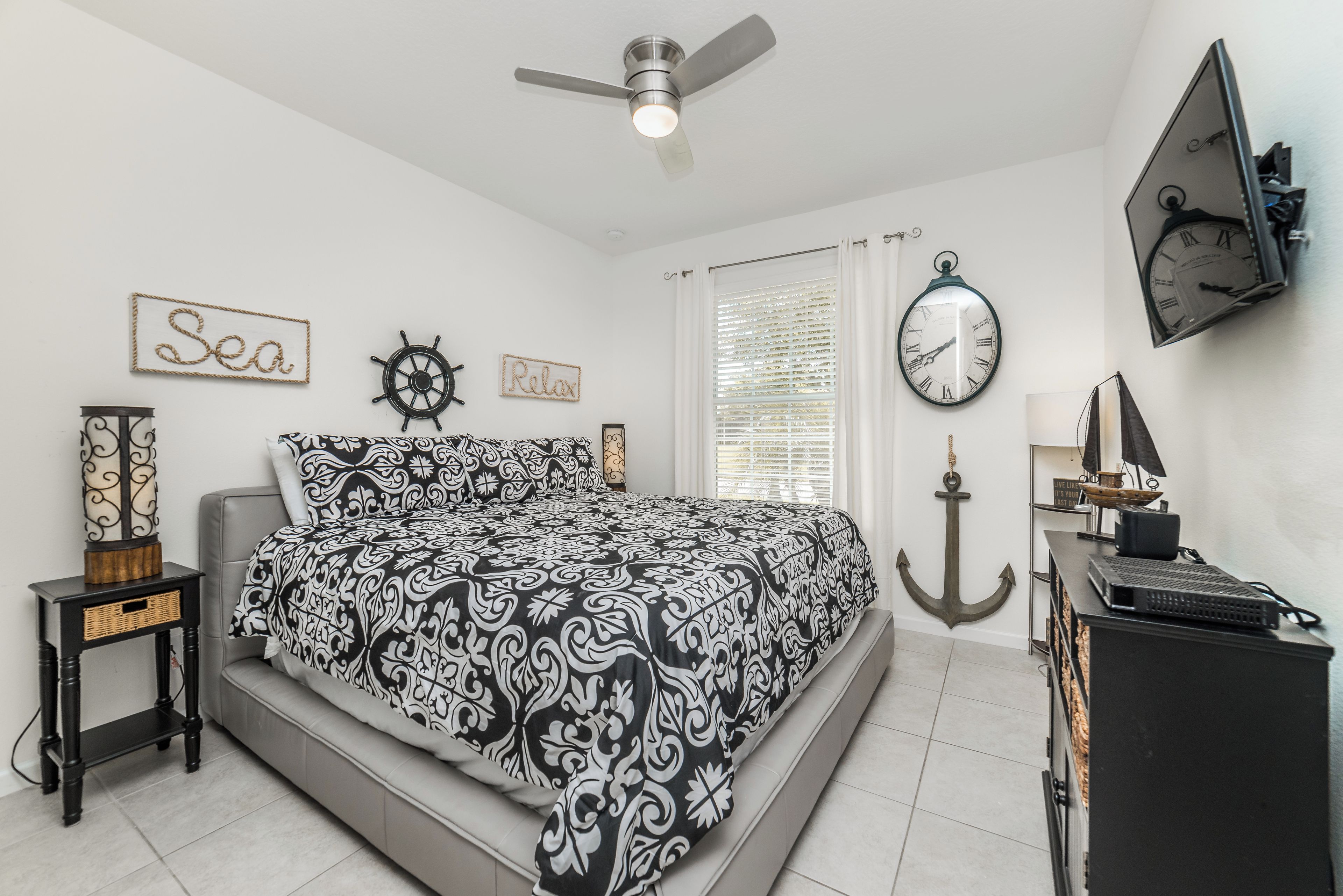 A bedroom with a bed, a ceiling fan, a wall clock, and nautical-themed decor.