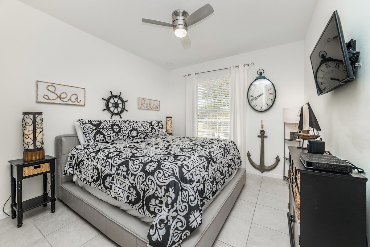 A bedroom with a bed, a ceiling fan, a wall clock, and nautical-themed decor.