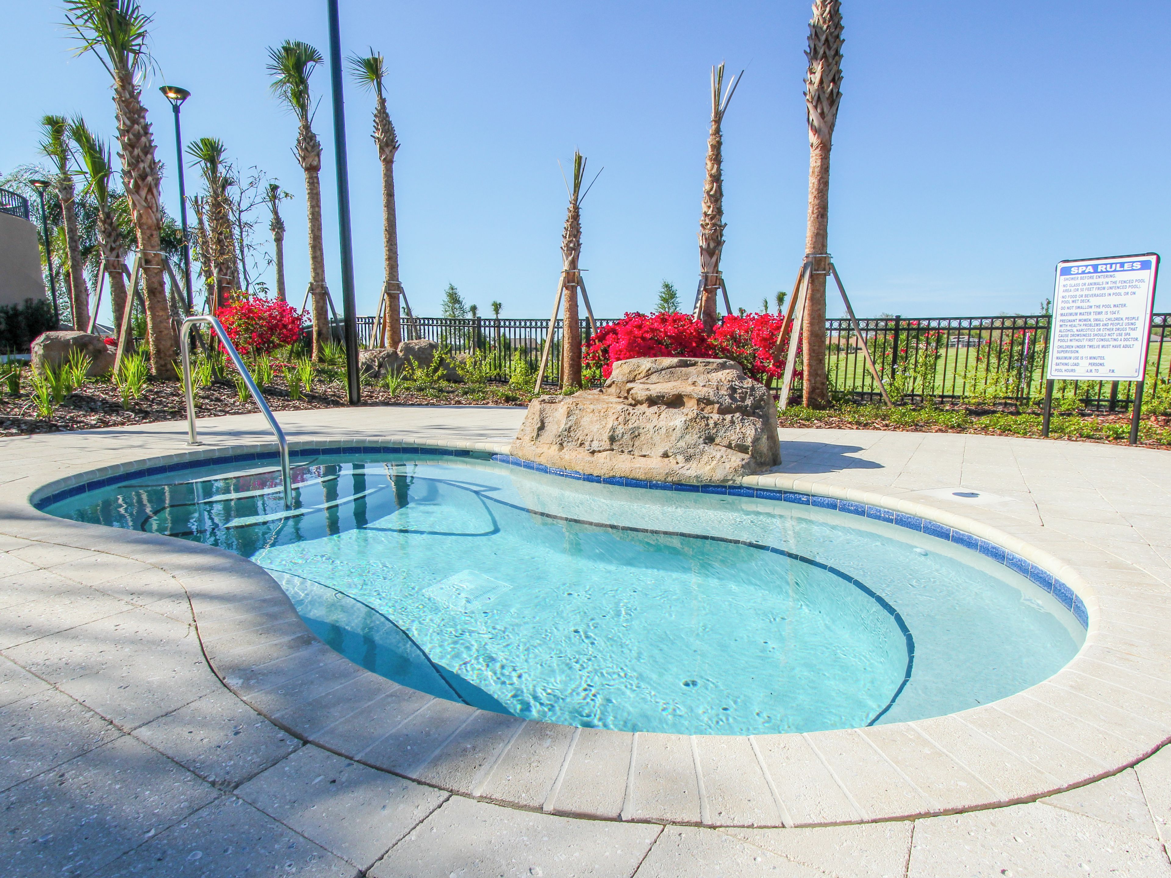 A swimming pool with a stone edge, surrounded by palm trees and a fence.
