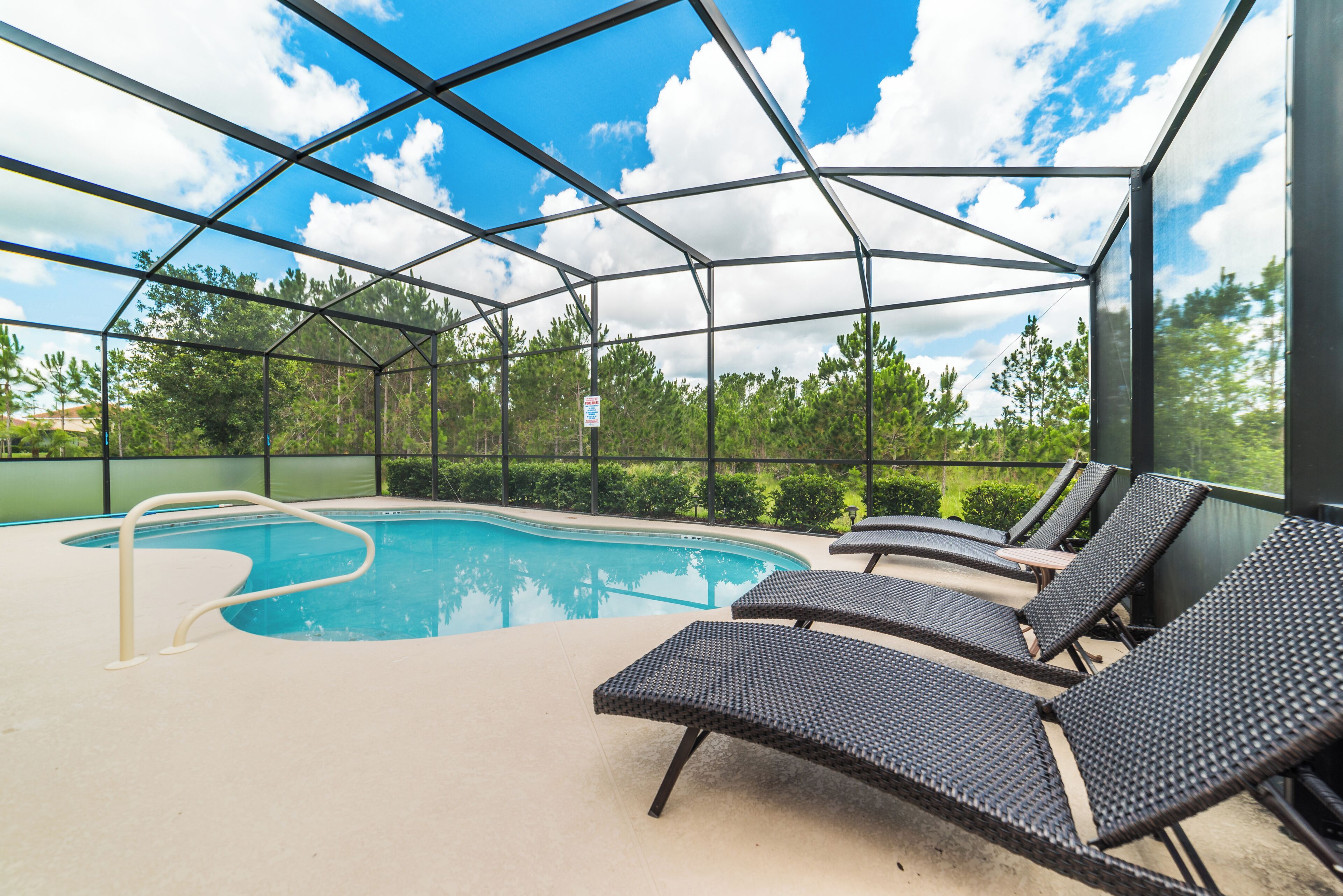 An indoor pool with clear glass walls, lounge chairs, and a view of trees and sky.
