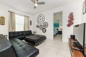 A modern living room with a sectional sofa, ottoman, wall clocks, and a television. - Solterra Resort Homes (Davenport)