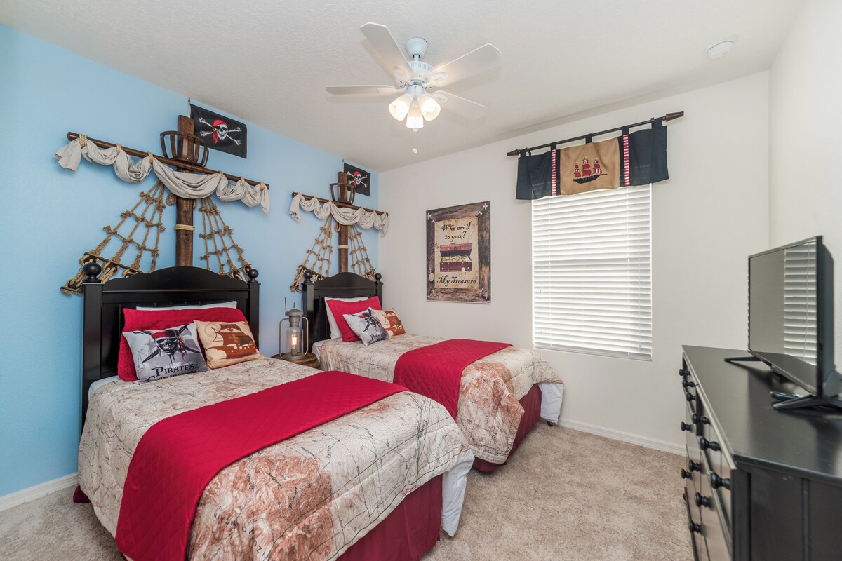 A bedroom with two beds, a ceiling fan, a dresser, and nautical-themed decorations.