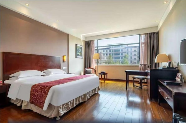 Une chambre d’hôtel avec un grand lit, un bureau, une chaise, une télévision et une fenêtre avec des rideaux.