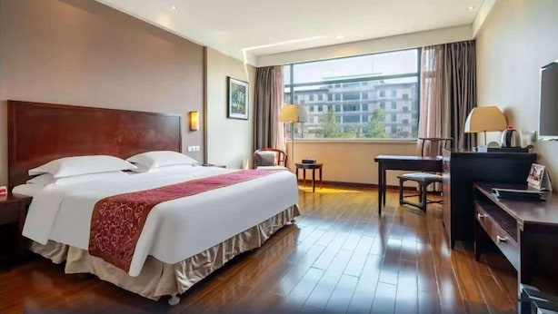 A hotel room with a large bed, a desk, a chair, a TV, and a window with curtains. - Ramada By Wyndham Suzhou Luzhi (Suzhou)