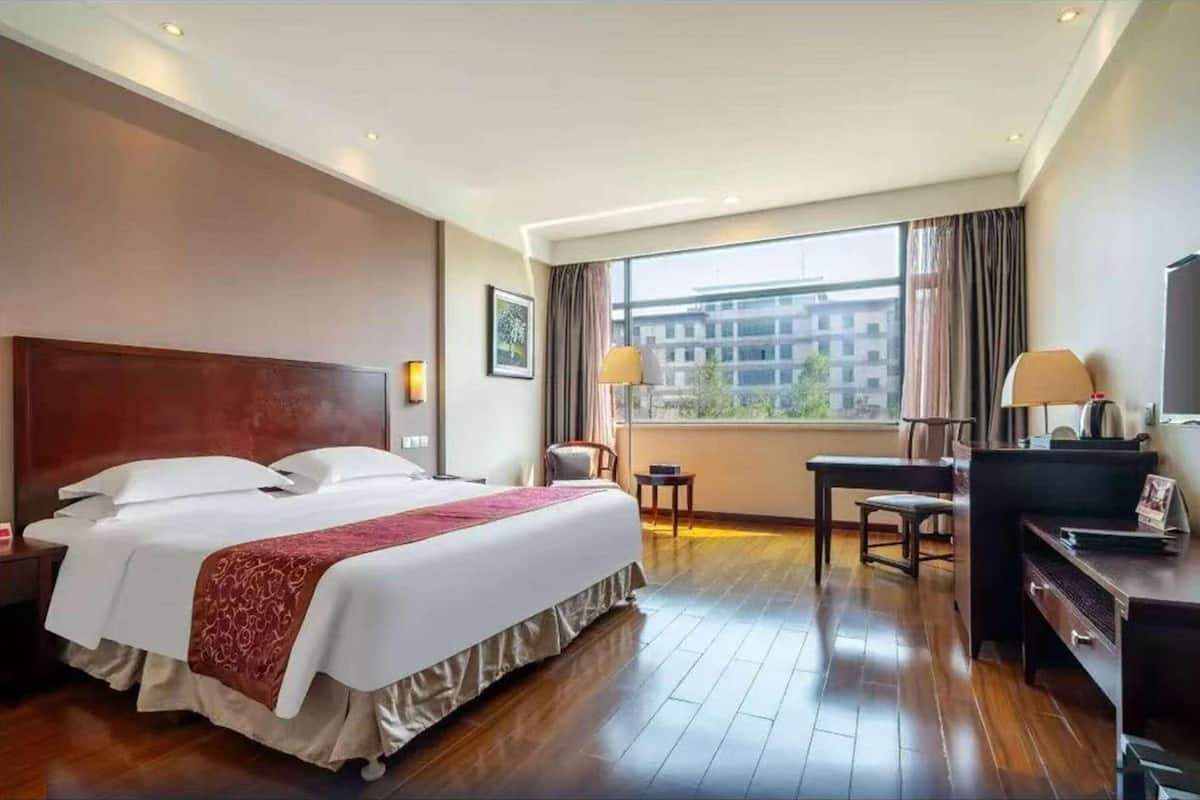 Een hotelkamer met een groot bed, een bureau, een stoel, een televisie en een raam met gordijnen.