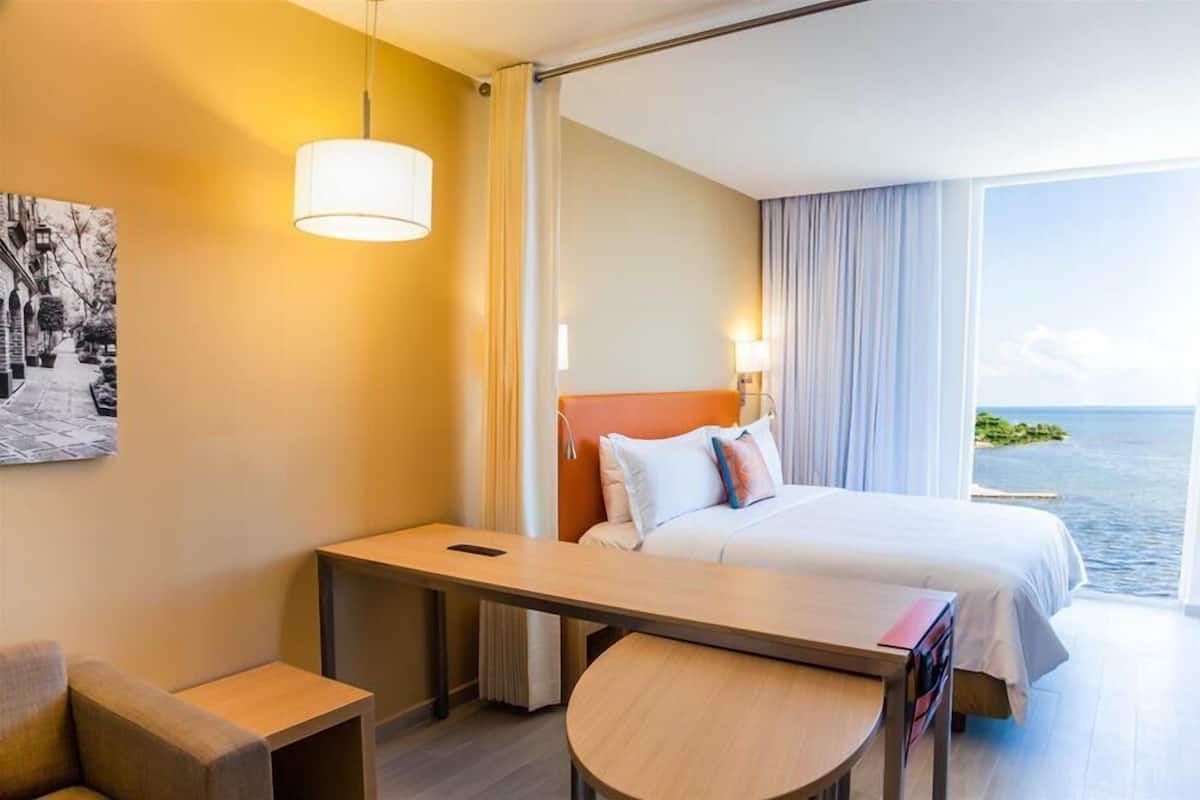 A hotel room with a bed, bedside table, chair, and a view of the sea.