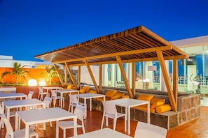 Een buitenruimte met tafels en stoelen, een houten pergola en uitzicht op de stad.