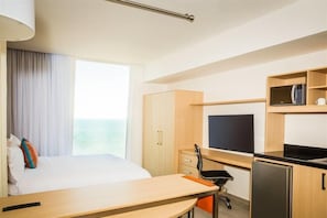 Hotellihuone, jossa on sänky, työpöytä, televisio, mikroaaltouuni ja jääkaappi.