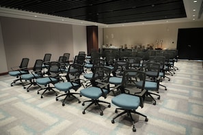 A conference room with rows of office chairs, a long table, and a bar area with stools.