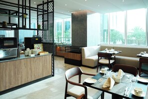 A modern hotel dining area with a wooden counter, seating arrangements, and large windows. - Novotel Riyadh Al Anoud (Al Muzahimiyah)