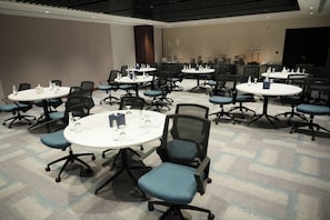 Une salle de conférence dotée de plusieurs tables et de chaises, ainsi que de bouteilles d’eau et de blocs-notes.