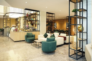 A modern hotel lobby with a reception desk, seating area, and decorative shelves.