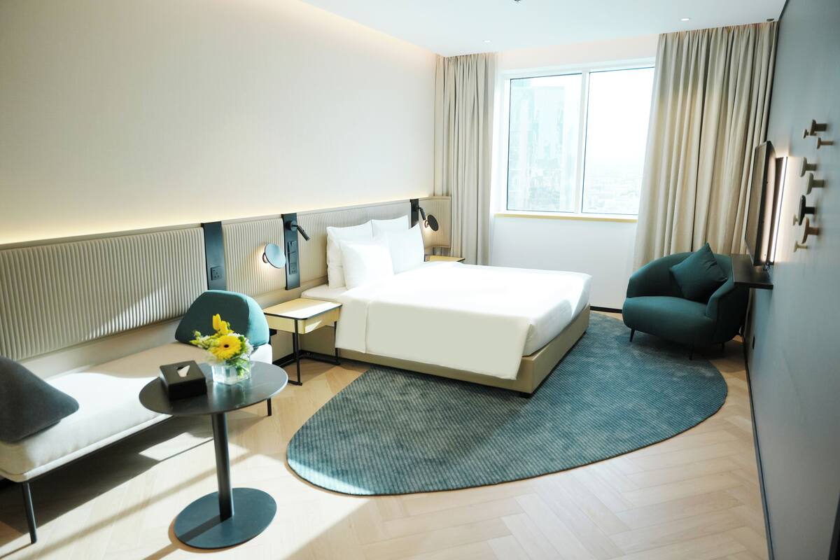 Une chambre d’hôtel avec un lit, une table de chevet, une lampe, une chaise et une vue sur la ville par la fenêtre.
