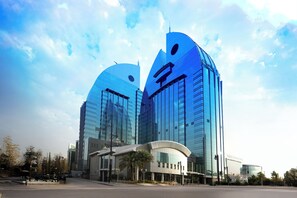 A modern hotel with a distinctive curved facade and a prominent logo. - Novotel Riyadh Al Anoud (Al Muzahimiyah)